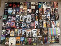 Photo showing around 55 VHS tapes from various movies and TV series laid out, visible cover art and titles.