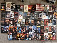 Mixed VHS collection showing multiple Rocky boxed set tapes, Rambo, Stallone films, Robocop 1 and 2, Die Hard series, and other action/thriller classics
