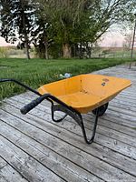 Side view of yellow MTD wheelbarrow on wooden deck with green grass background.