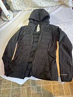 Front view of black Lululemon hooded jacket laid flat showing full-zip and quilting