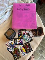 Pink binder labeled Red 2022 Hockey Cards beside stacks of Magic and sports cards