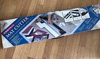 Retail box of Logan Compact Mat Cutter showing product image and specifications