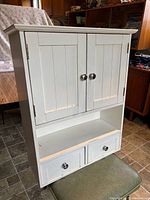 Front view of closed cabinet showing shaker doors, open shelf, two drawers
