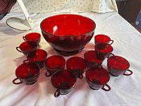 Punch bowl with twelve matching ruby red cups on white surface