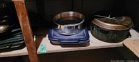 Shelf view showing blue lidded casserole dish with metal ring and large cast iron pot with lid