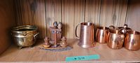 Clear view of the entire lot showing the brass plant pot, wooden peanut character set on a wooden base, and six copper cups arranged on a wooden shelf.