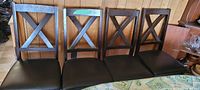 Photo of four dark brown wood dining chairs with leather-like seat covers, showing their overall condition and style.