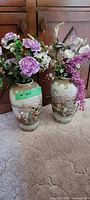 Front view of two vintage Japanese ceramic vases filled with silk flowers in varying shades of purple, pink, and white placed side by side on carpeted floor.