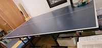 Blue ping pong table fully opened showing surface and legs with caster wheels below.