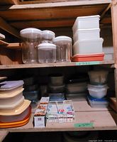 Various plastic containers arranged on two shelves showing round, square, and rectangular shapes with lids of various colors.