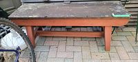 Photo from a low angle showing the entire top and front of rustic wooden bench, highlighting the worn top surface and rust-colored legs.