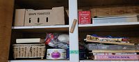 Shelf view with assorted sewing supplies including a cardboard box labeled 'Grape Tomatoes', woven basket, thread packages, booklets, and small sewing items.