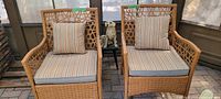 Pair of rattan chairs with striped cushions side by side with small black stool and dog figurine in the middle.