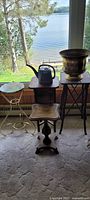 The entire lot showing the watering can, brass pot, wooden table, metal plant stand with marble top, and small wooden stools/stands all placed near a window with a lake view.
