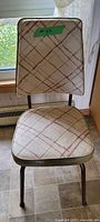 Front view of vintage upholstered chair showing cream and multicolor patterned fabric with olive trim and backrest, metal legs visible