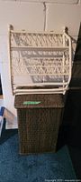 Photo of white rattan shelf on wall above brown wicker hamper on blue carpet