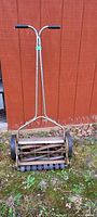 Front full view of vintage manual reel lawn mower showing metal handle with black grips and cutting blade assembly.