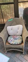 Full front view of taupe colored vintage rattan rocking chair with floral round seat cushion and white tufted back cushion.