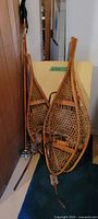Pair of vintage wooden snowshoes leaning against a yellow board and wooden wall along with two wooden poles beside them