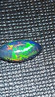 Close-up photo of a marquis cabochon shaped black opal showing bright multicolored flashes of green, red, and orange.