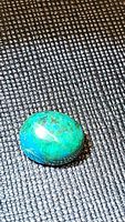 Close-up of oval chrysocolla cabochon showing its blue-green color and polished surface on black textured background.