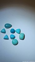 Nine natural robin's egg blue turquoise cabochons varying in shape and size laid out on a white surface.