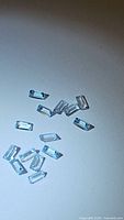 13 small baguette cut baby blue topaz gemstones with a pale blue color and good clarity arranged on a plain surface.
