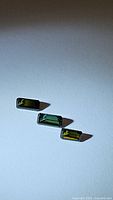 Three octagon cut green tourmaline stones placed side by side on a white surface with natural lighting showing stone colors and facets.