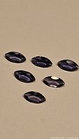 Six marquis cut purple iolite gemstones arranged on a flat surface, showing faceted cuts and clarity