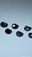 Top-view photo of six individual natural blue sapphires scattered on a flat surface under bright light to show their round cut and deep blue color.