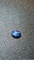 Close-up photo of a 1.16 carat natural blue star sapphire oval cabochon showing the distinct six-ray star effect on a textured background.