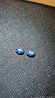Two oval blue star sapphire cabochons showing clear six-rayed star asterism on textured surface background.