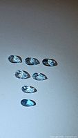 Seven pear-shaped aquamarine gemstones laid out on a light surface under direct lighting, highlighting their blue color and clarity.