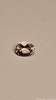 Close-up of a single oval cut champagne morganite gemstone on a neutral background showing the stone's facets and color.