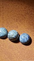 Three polished natural dumortierite gemstones with blue and gray hues laid on a brown textured surface.