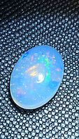 Close-up photo of oval-shaped natural Ethiopian opal cabochon showing multicolored flashes on a textured dark background.