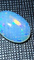 Oval cabochon cut natural Ethiopian opal with bright purple, blue, and green play of color on black textured background.