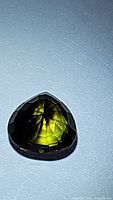 Close-up image of a green tourmaline pear-cut gemstone on a plain surface showing its color and facets.
