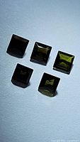 Five natural green tourmaline princess cut gemstones arranged in two rows on a white background, showing color and cut details.