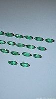 Photo of multiple natural marquis cut emerald stones arranged on a flat surface with visible clarity and green color.