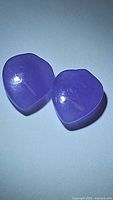 Pair of natural lavender jade stones cut into a fancy spade shape with cabochon finish shown under light, highlighting their color and surface.