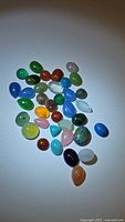 Natural mixed polished gemstones in various colors and sizes on a white background.