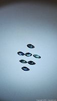 Seven marquis cut multicolored sapphires scattered on a white background, showing various colors and clarity.