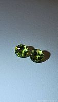 Pair of round cut natural peridot stones on white surface, showing bright apple green color, facets visible