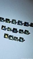 Close-up image showing rows of small princess cut sapphires with multicolored hues including green, blue, and yellow tints.