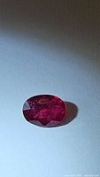 Oval cut natural ruby gemstone on a white background showing deep red color and clarity inclusions.