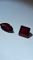 Photo showing two natural rubies with mixed cuts on a white surface, marquise and square shape visible.