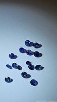 15 loose natural blue sapphires of varying sizes arranged on white background showing round faceted cuts with high polish and brilliance.