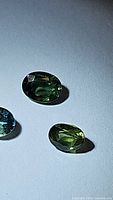 Close-up photo of three oval faceted sapphires in different colors (green, light green, blue) on a plain background.
