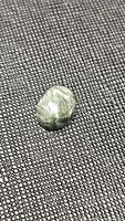 Single polished oval seraphinite cabochon on textured fabric background showing feather-like chatoyancy and green color.